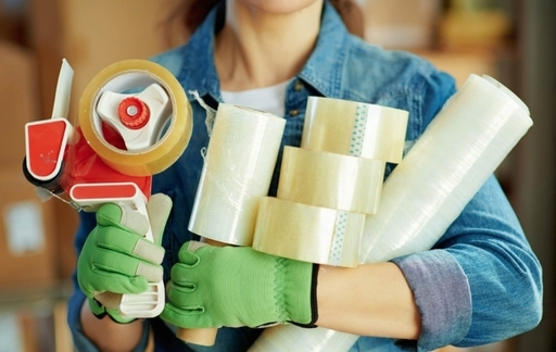 Woman holding various packing materials including plastic packing strip, metal packing strip, packing tool, aluminium tape, duct tape, masking tape, double sided tape, stretch wrap, and bubble wrap at Starlinks